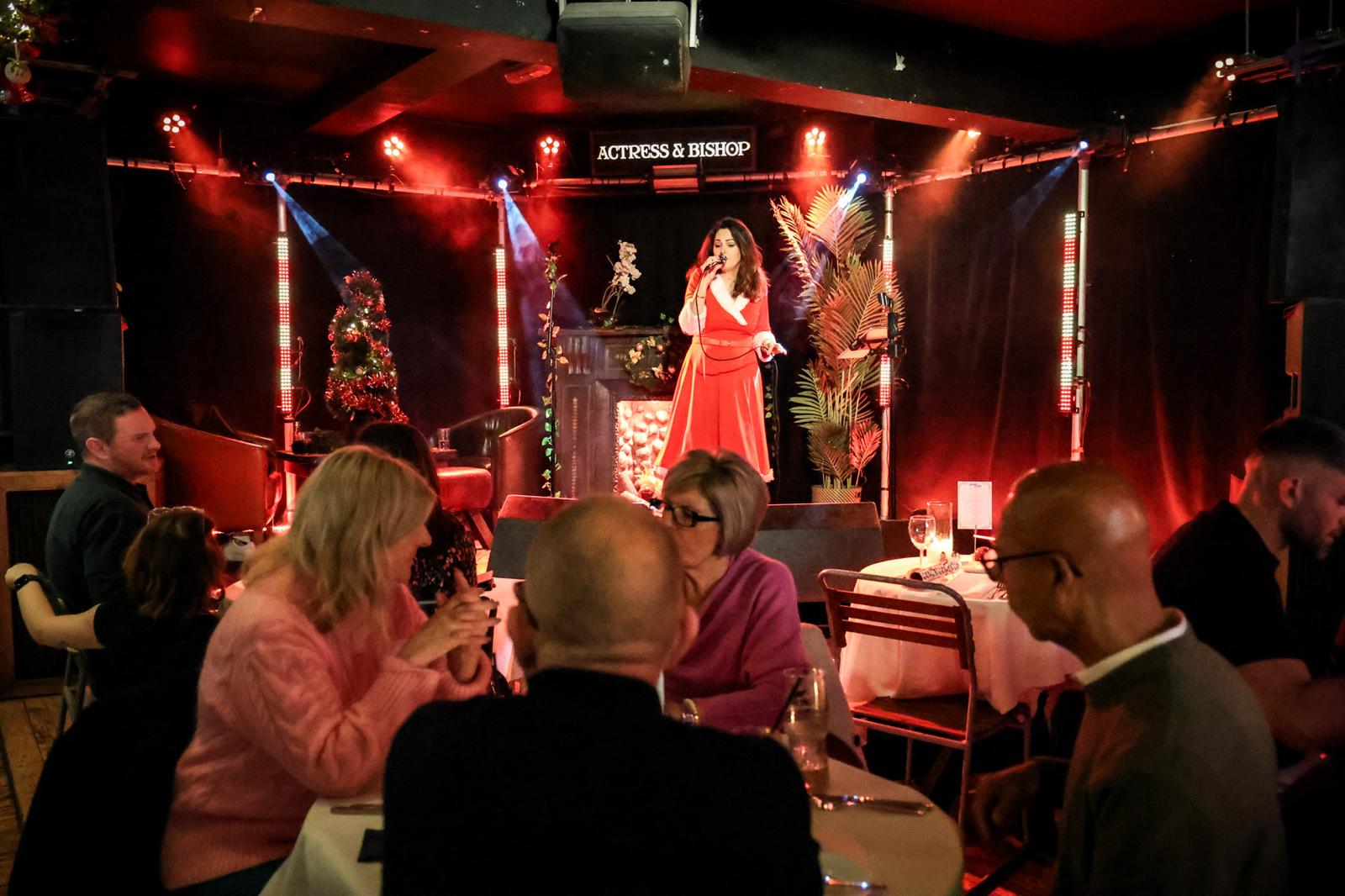 Singer performing on stage beside a lit Christmas tree in the bar